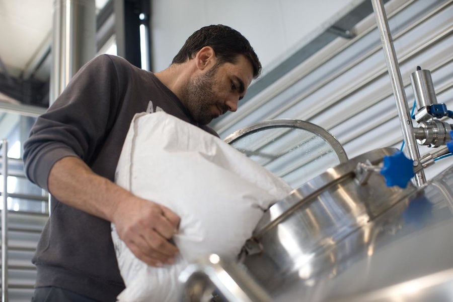 man οverturning sack with barley corns into beer brewing machine at Cretan Brewery plant